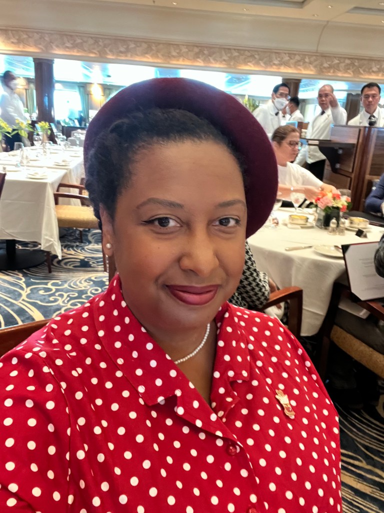 A photo of Gigi in a red and white polka dot outfit an red hat and pearl necklace, smiling into the camera